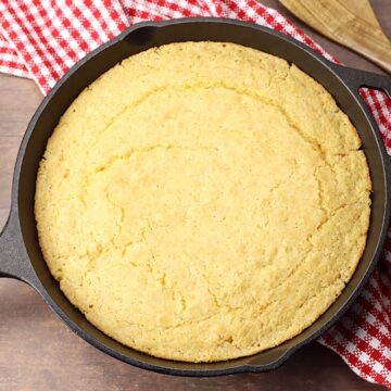 Skillet cornbread on a wood counter top with red checked towel.