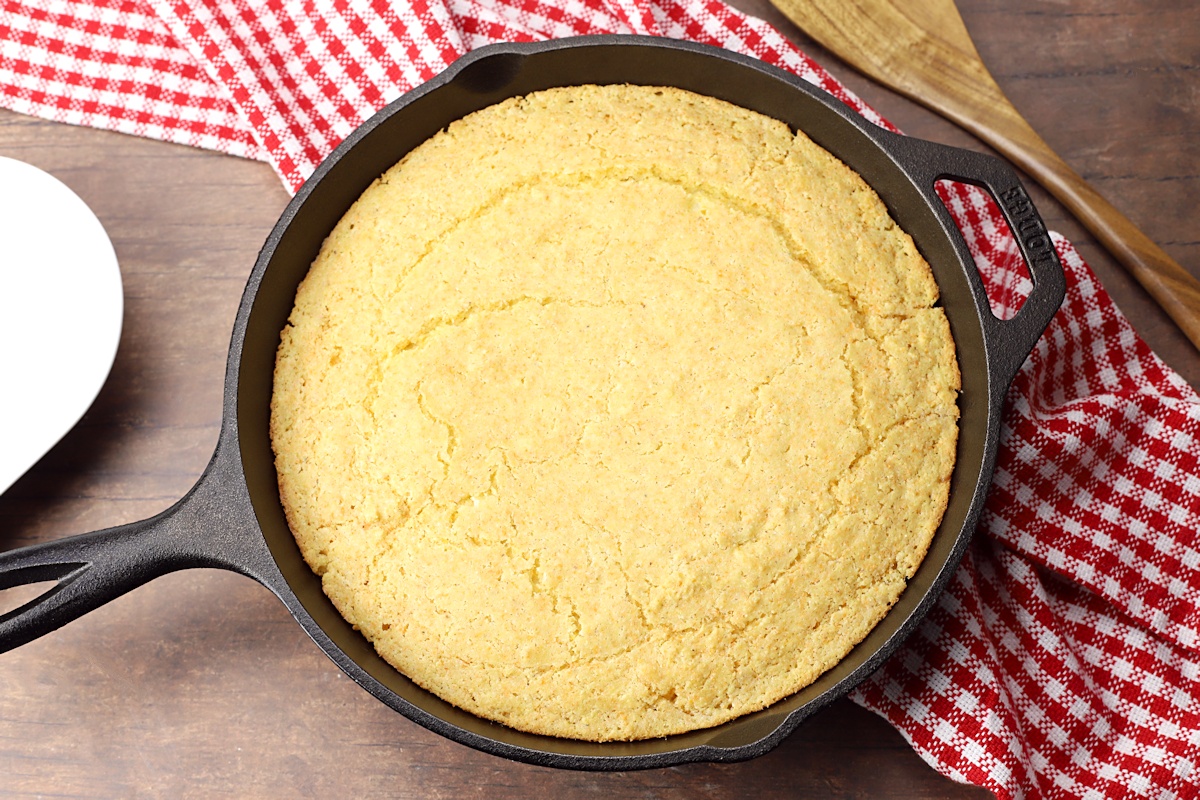 Skillet cornbread on a wood counter top with red checked towel.