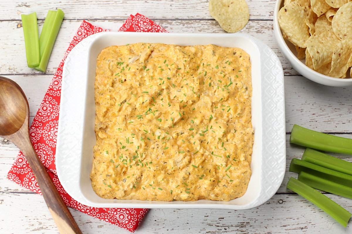 Crock pot buffalo chicken dip in a casserole dish on a white counter top with chips and celery.