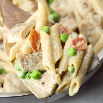 A wooden spoon scooping pasta in alfredo sauce.