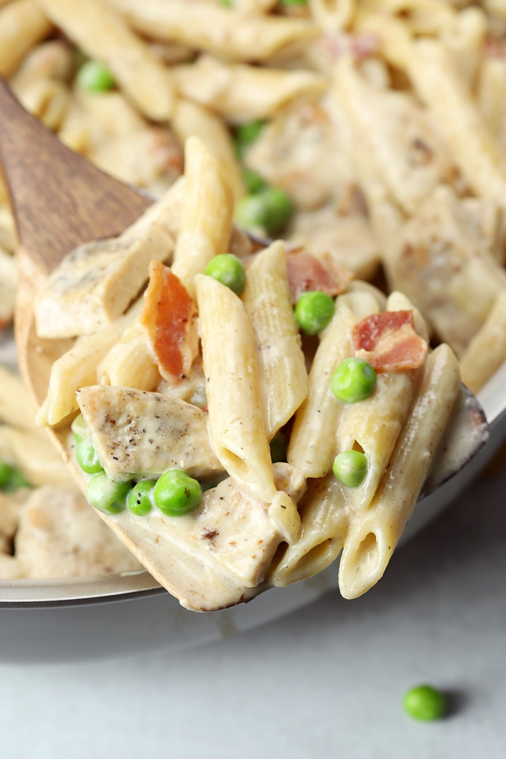 A wooden spoon scooping pasta in alfredo sauce.