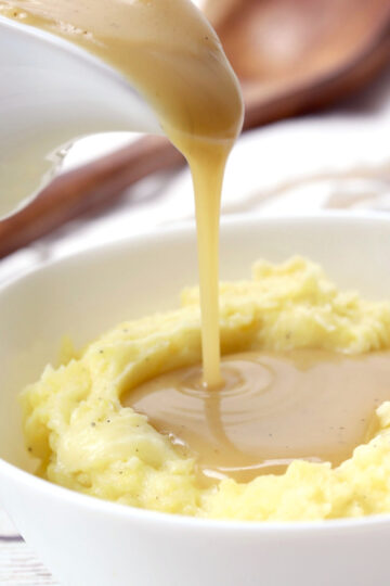 Pouring gravy over a bowl of mashed potatoes.