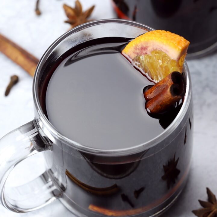 An orange slice and cinnamon stick in a glass of mulled wine.