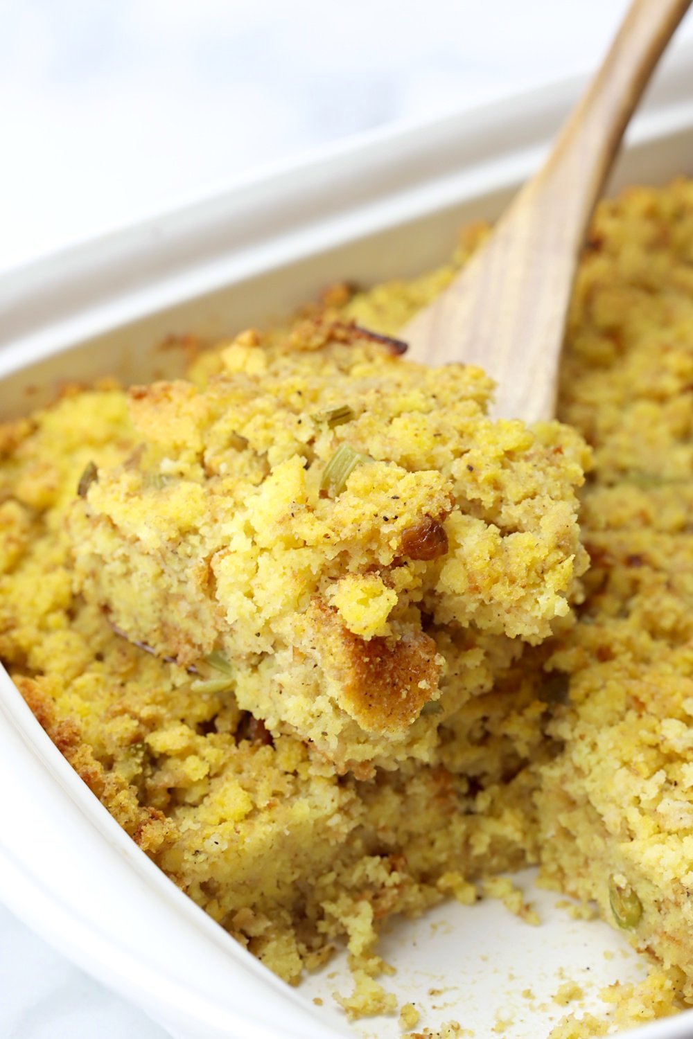 A wooden spatula lifting a serving of cornbread dressing from a pan.