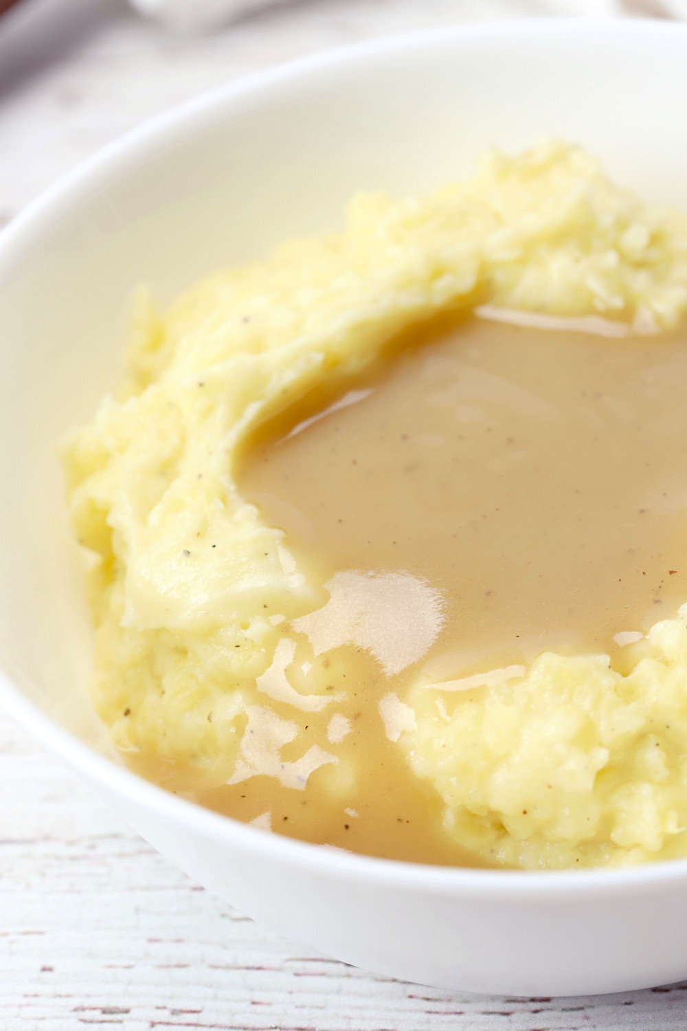 White bowl filled with mashed potatoes and gravy.