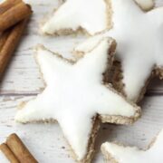 Zimtsterne cinnamon star cookies on a white counter top with cinnamon sticks.