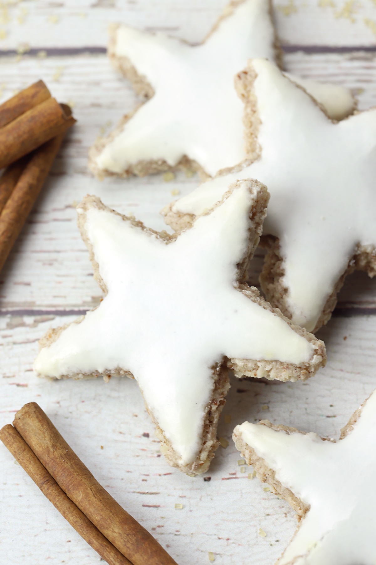 Zimtsterne cinnamon star cookies on a white counter top with cinnamon sticks. 