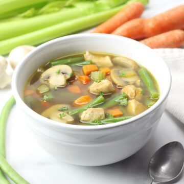 White bowl filled with soup, celery and carrots in the background.