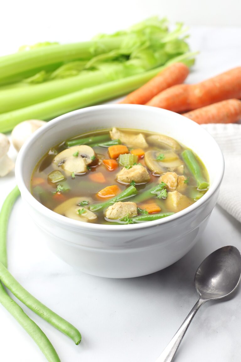 White bowl filled with soup, celery and carrots in the background.