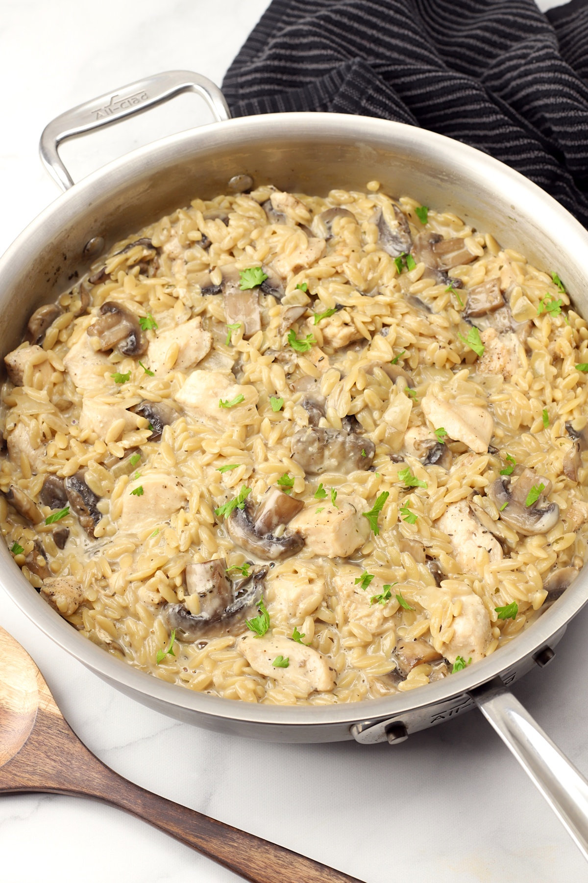 A saute pan filled with chicken, mushrooms, and orzo pasta.
