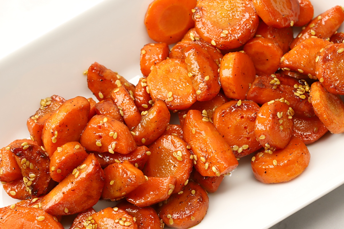Sliced carrots coated in honey and tossed in sesame seeds on a white serving plate.