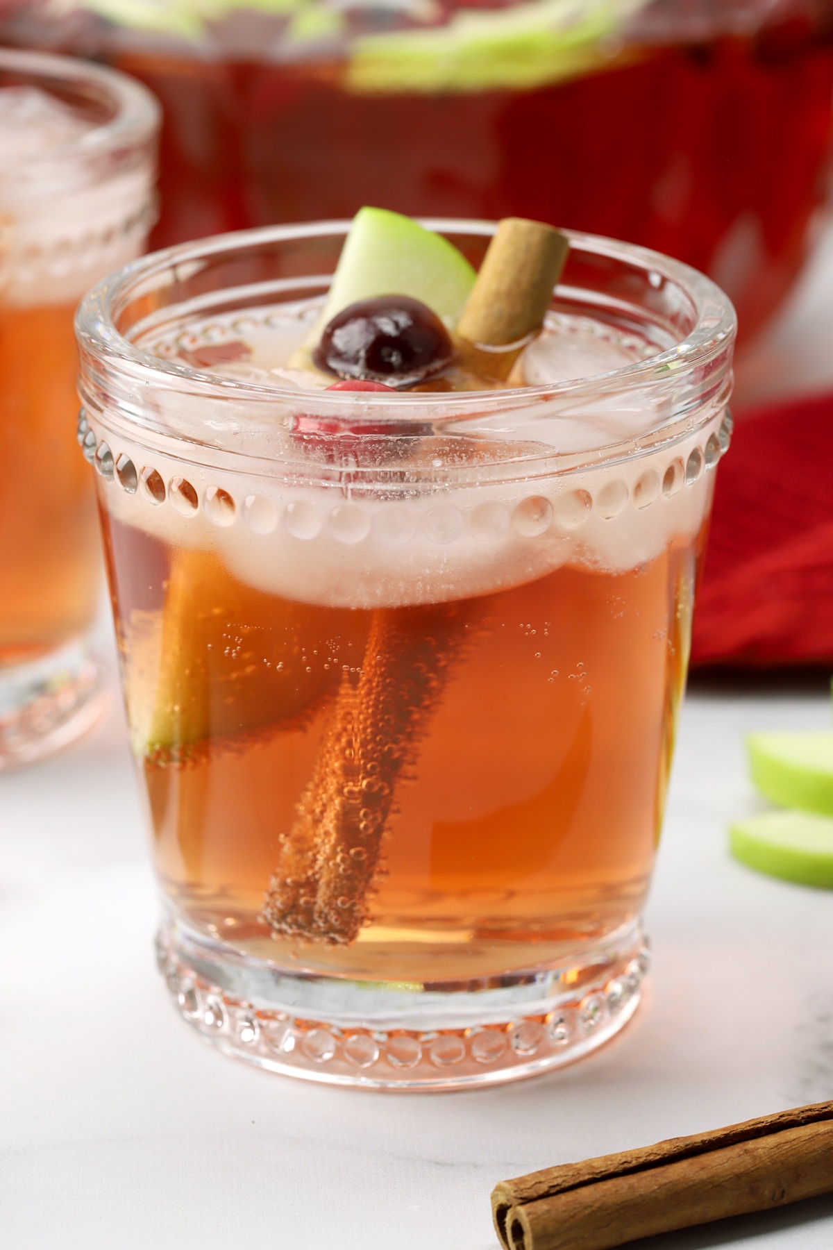 A glass with cinnamon stick, apple wedge, and punch.
