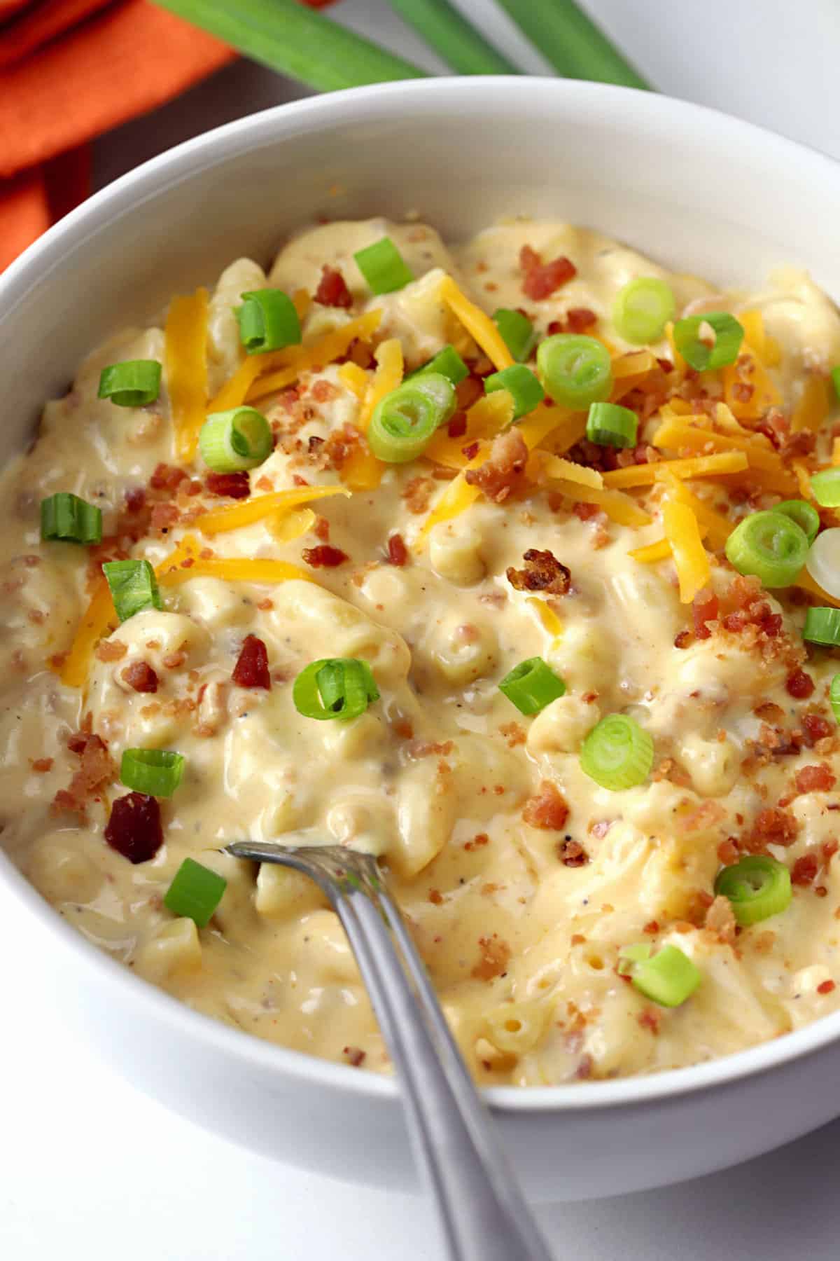 A white bowl filled with mac and cheese topped with green onions and bacon.