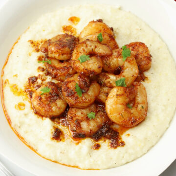 A white bowl filled cajun shrimp and grits.