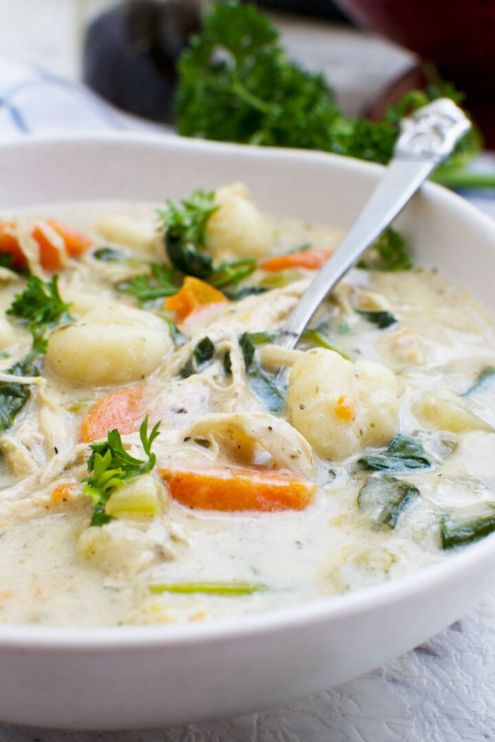 Soup with chicken, vegetabls, and gnocchi in a white bowl with a spoon.