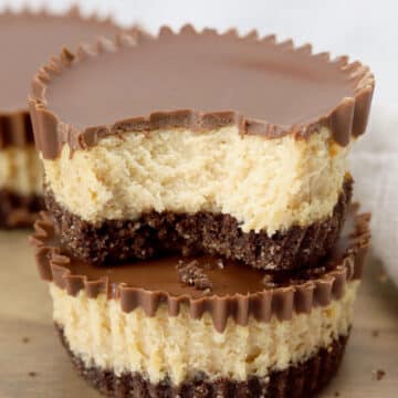 Two mini peanut butter cup cheesecakes stacked on a cutting board.