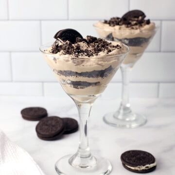 Two martini glasses with layers of chocolate and crushed cookies.