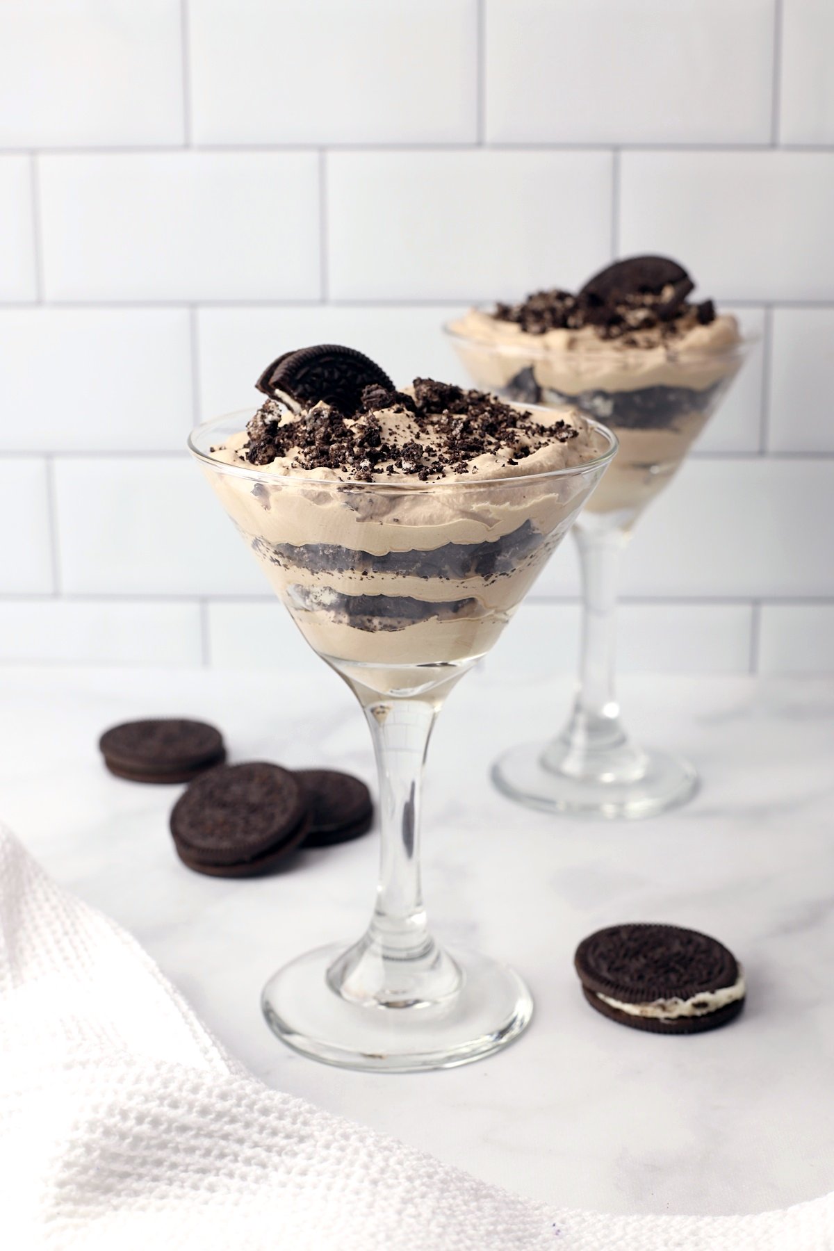 Two martini glasses with layers of chocolate and crushed cookies.