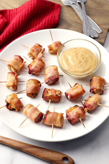 A plate filled with honey mustard bacon wrapped chicken bites on toothpicks with a bowl of mustard.