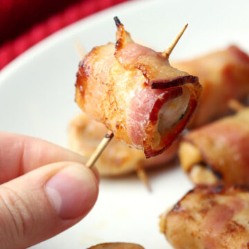 Someone holding a bacon wrapped chicken bite on a toothpick.