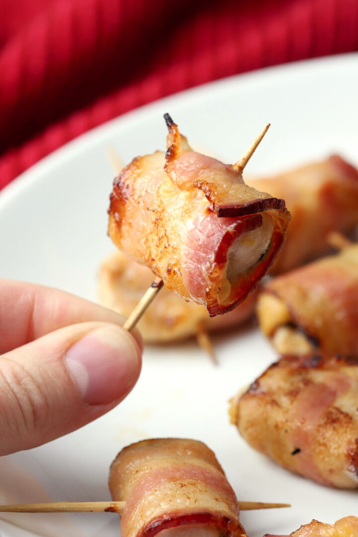 Someone holding a bacon wrapped chicken bite on a toothpick.