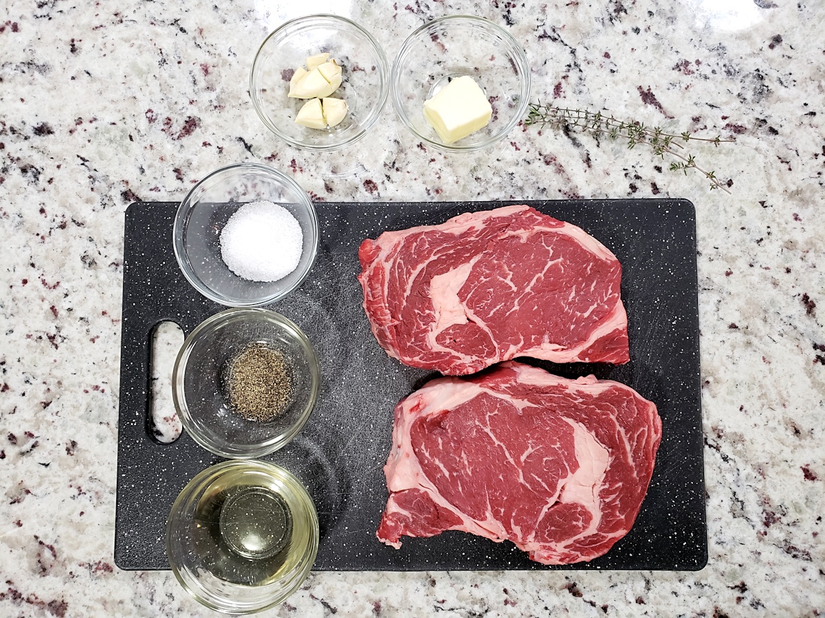 Ribeye steaks on a cutting board with salt, pepper, and oil.