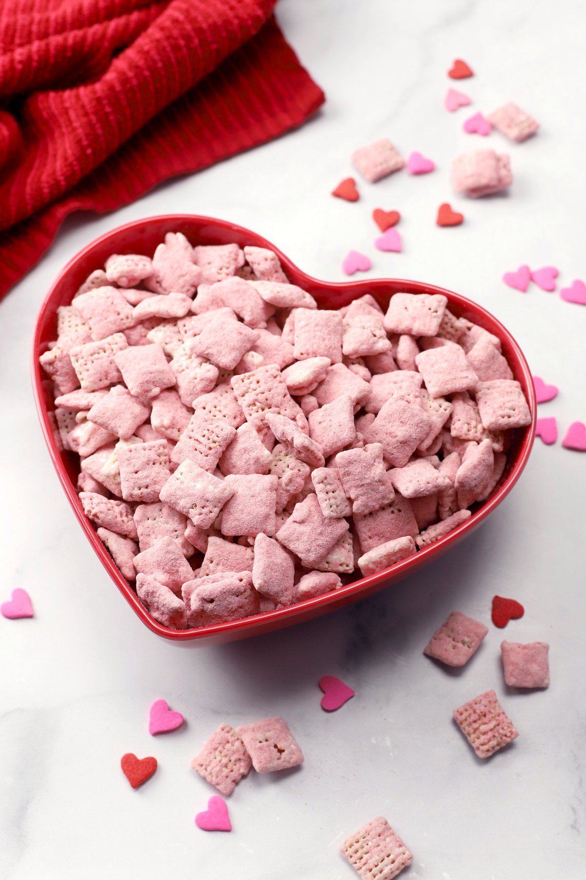 Red heart shaped bowl filled with pink chex mix.