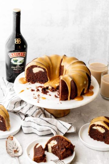 A sliced chocolate bundt cake with icing on top, next to a bottle of Baileys Irish cream.