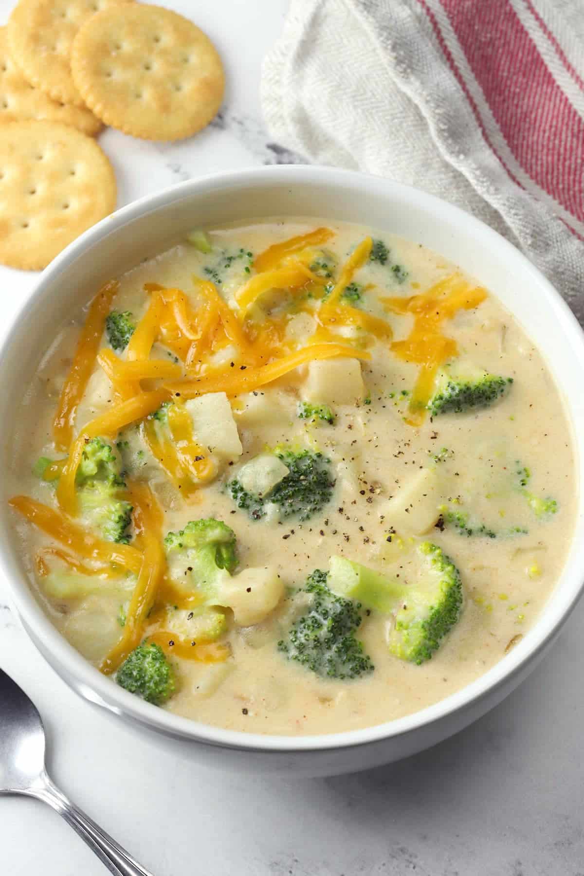 White bowl filled with broccoli potato soup, topped with shredded cheese.