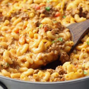 A wooden spoon scooping hamburger helper from a pan.