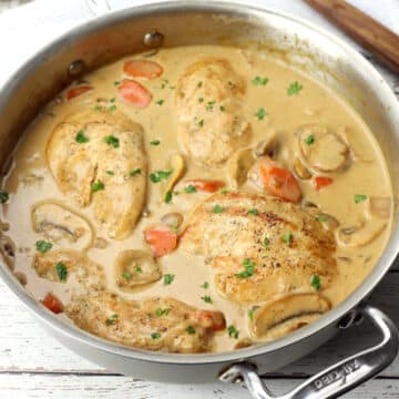 Finished chicken fricassee in a saute pan on a white wood counter top.