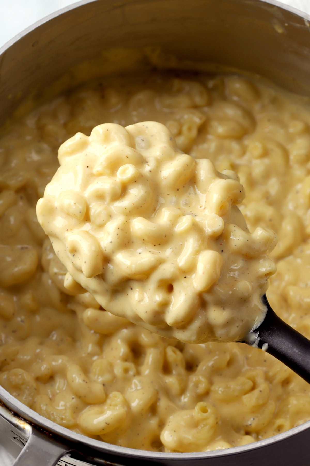 A large spoon scooping a serving of creamy mac and cheese from a pot.