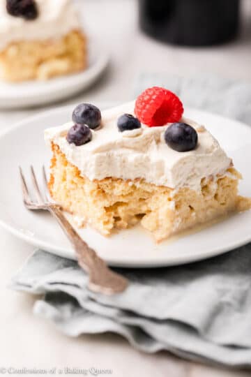 A slice of tiramisu on a white plate with a fork, garnished with fresh berries on top.