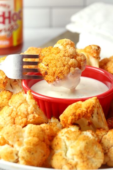 A fork dunking a piece of roasted cauliflower into ranch dressing.