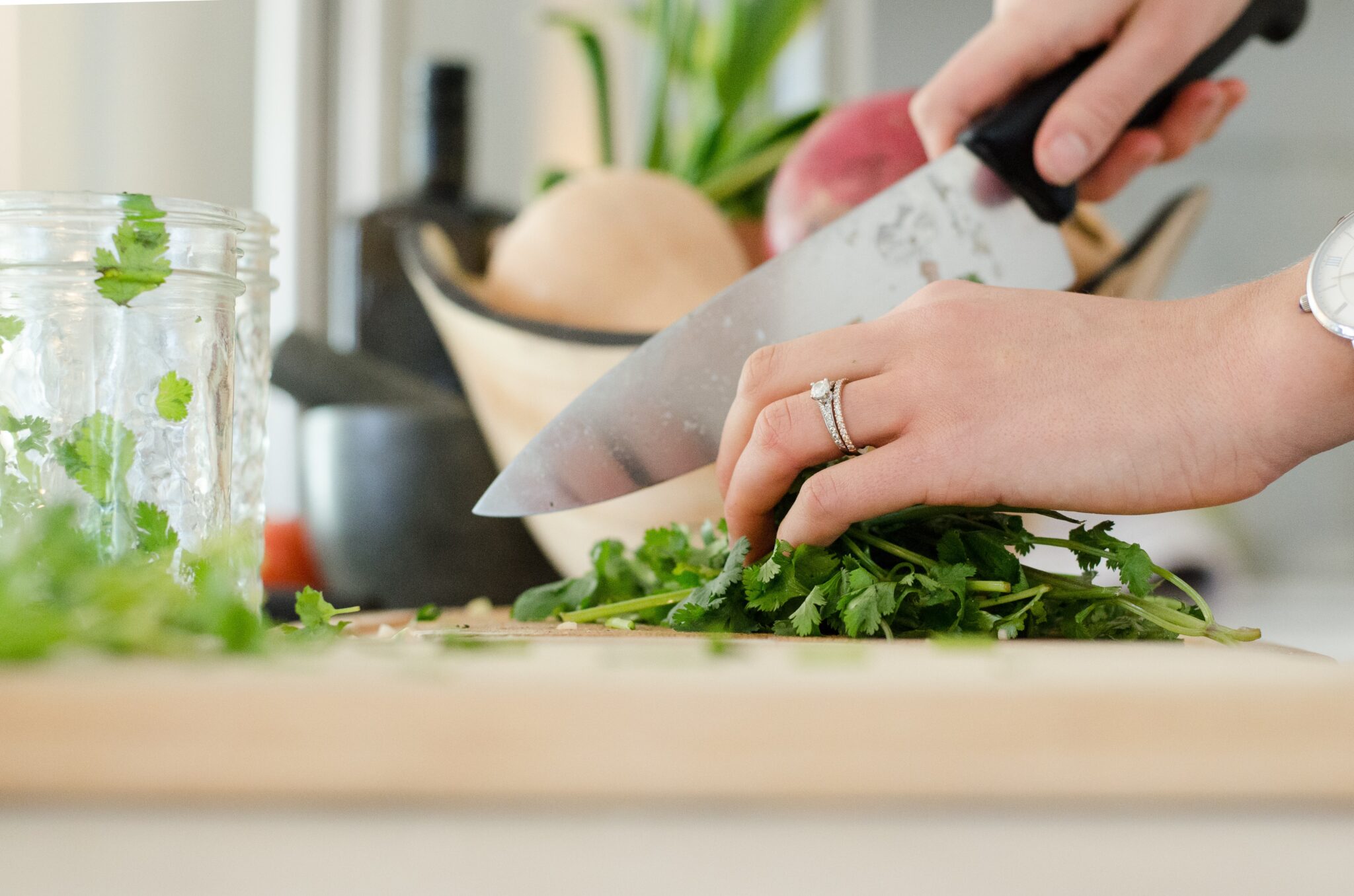 Hands holding a knife, chopping greens on a cutting board.