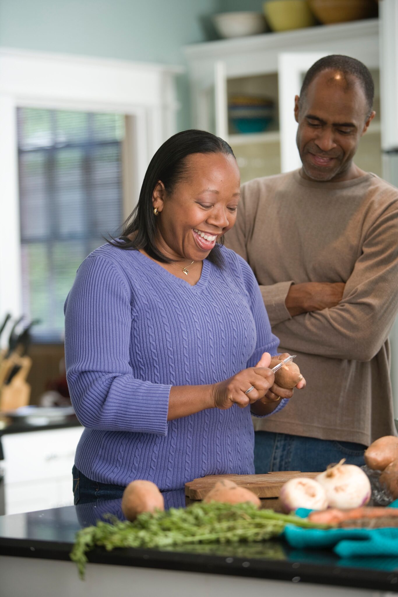 A woman peeling potatoes with man in kitchen.