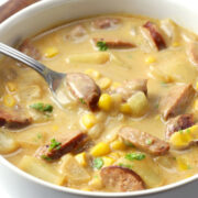 Chunky potato and corn soup with sausage and a metal spoon.