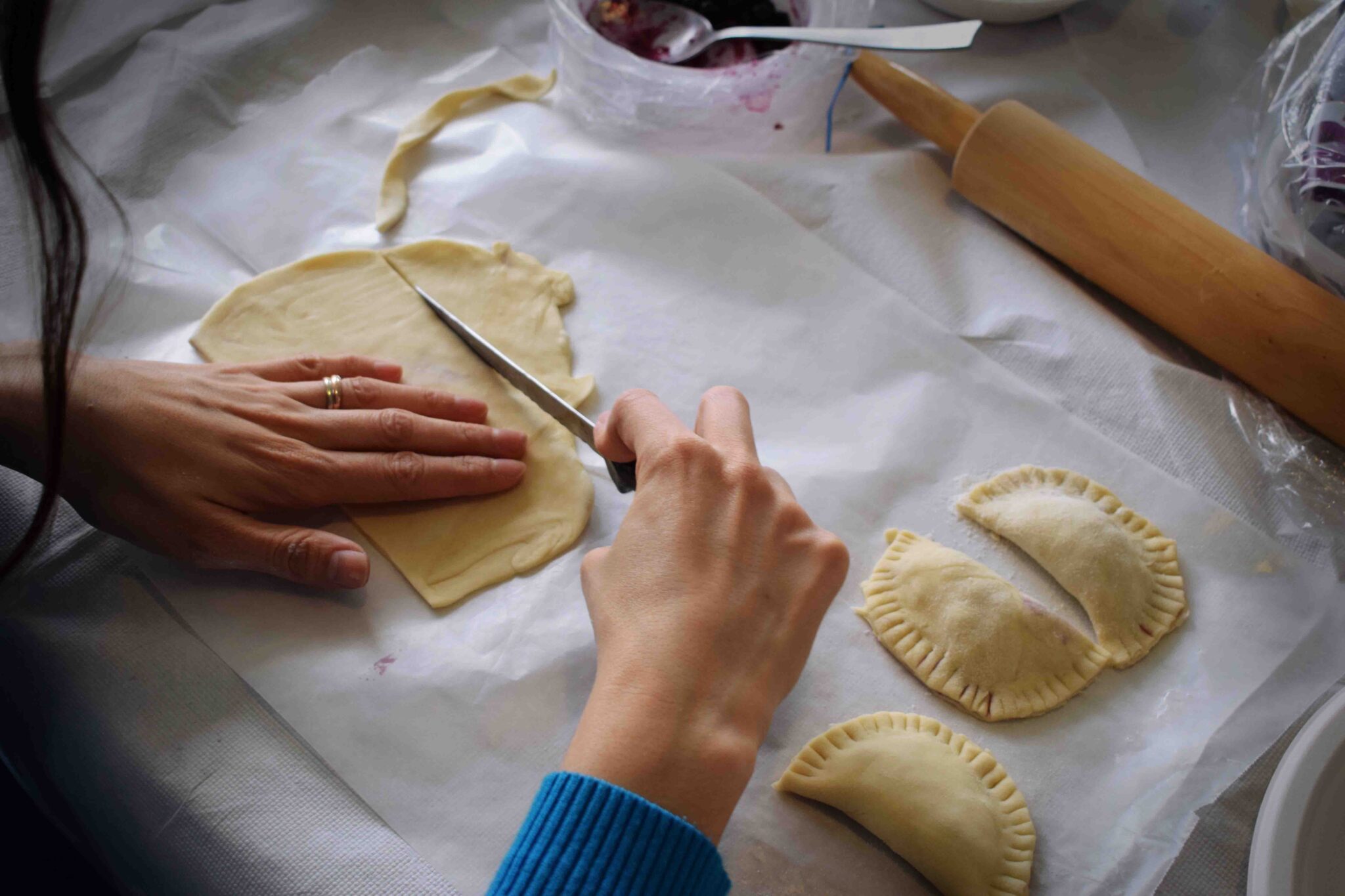 Hands cutting dough for empanadas.