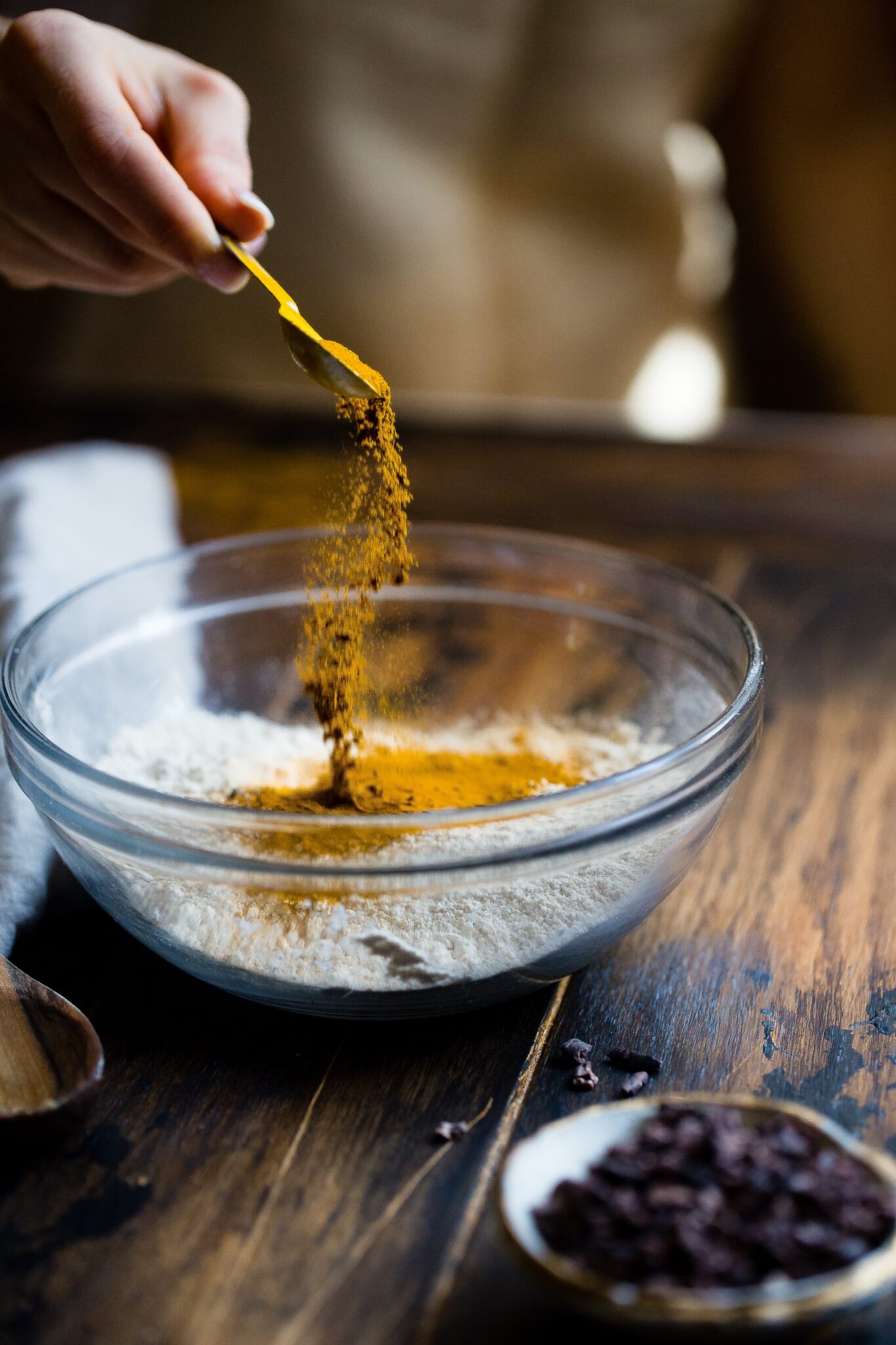 A hand pouring turmeric into a glass bowl.