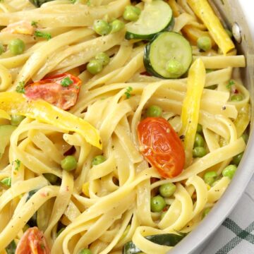 Close up of fettuccine noodles, tomatoes, and zucchini coated in a creamy sauce.