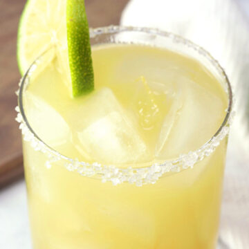 A pineapple margarita with salted rim and lime wedge.