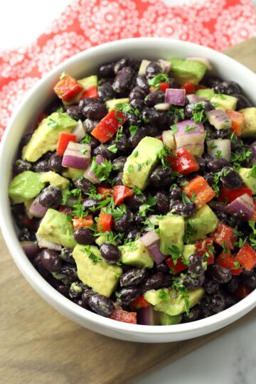 A white bowl filled with black beans, red peppers, and avocado.