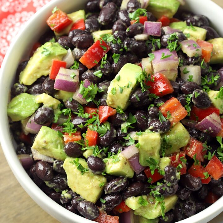 A white bowl filled with black beans, red peppers, and avocado.