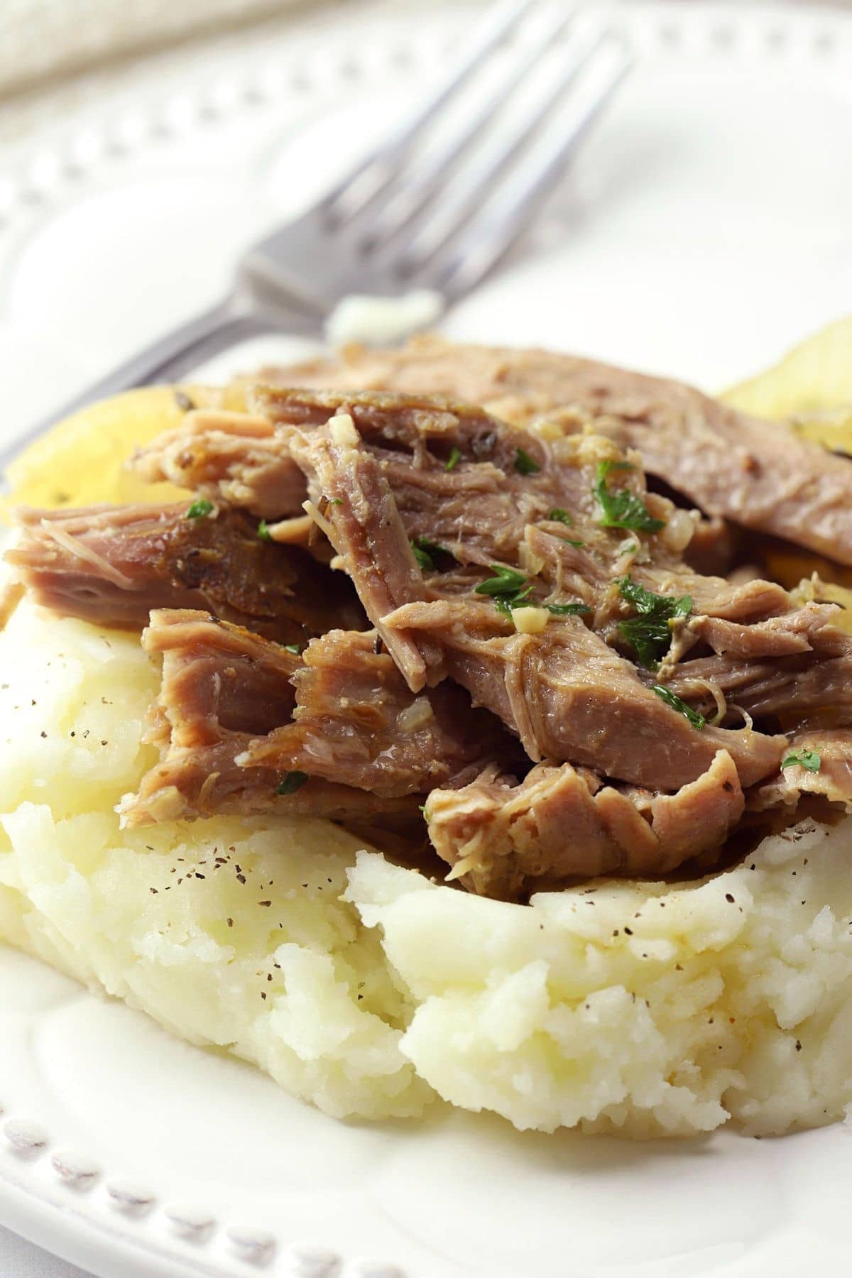 Garlic & herb slow cooker pork roast on a bed of mashed potatoes on a plate.