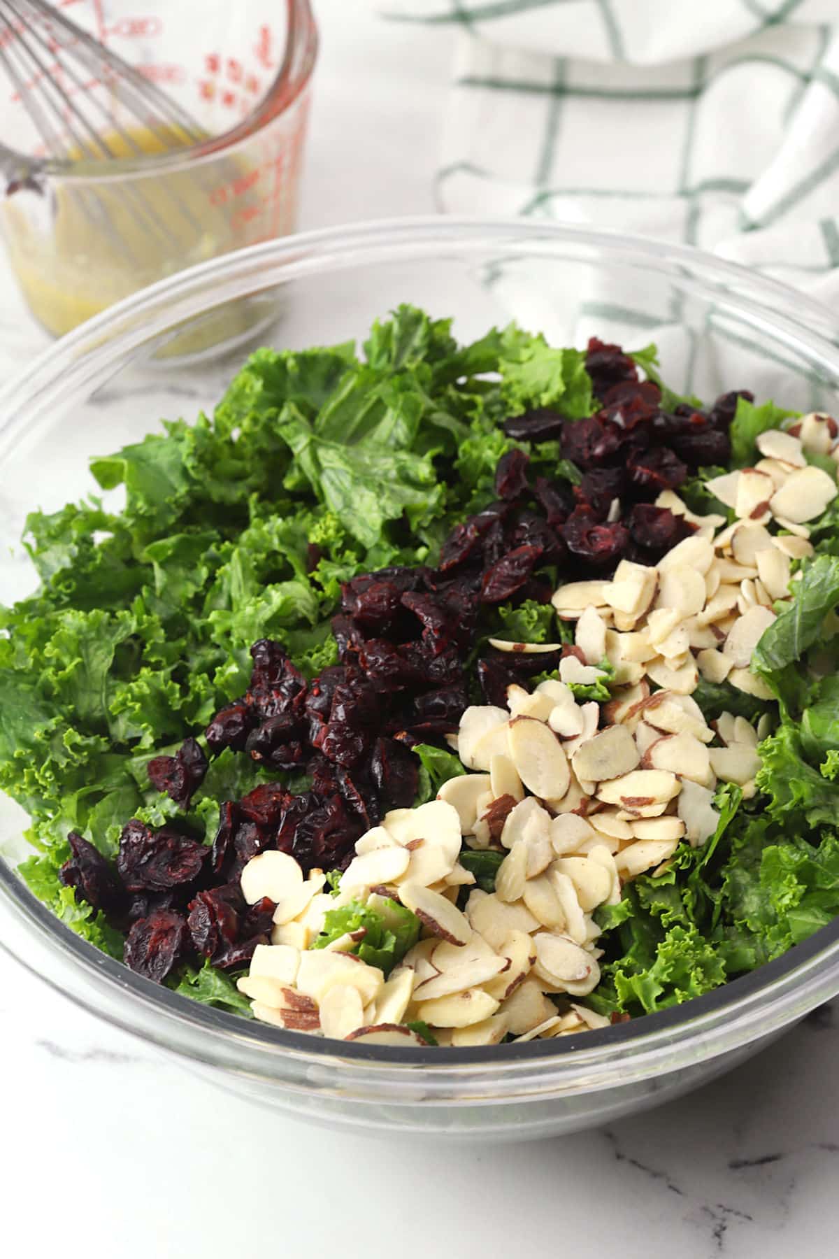 Kale cranberry salad ingredients in a large glass bowl.