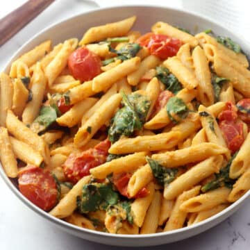 Bowl of penne pasta with spinach and cherry tomatoes.