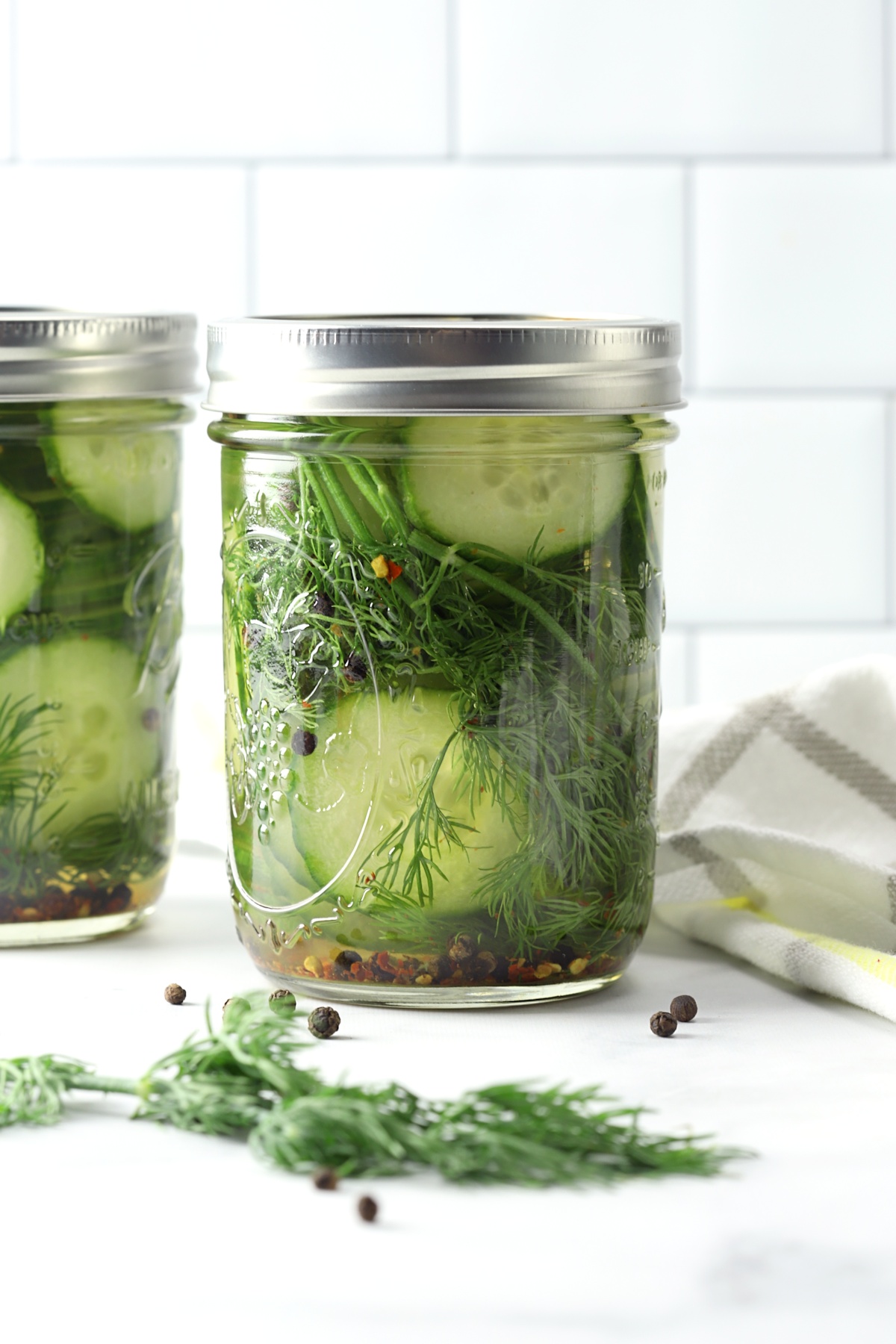 A mason jar of homemade pickles on a counter top with a kitchen towel.