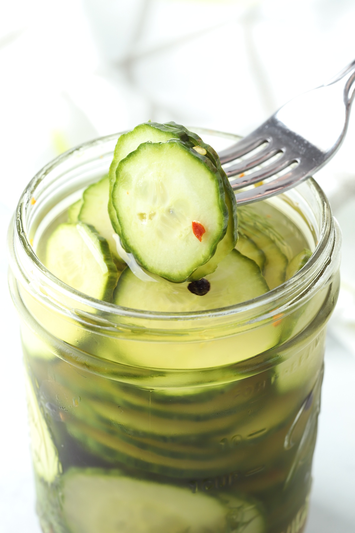 A fork piercing into pickles in a jar.