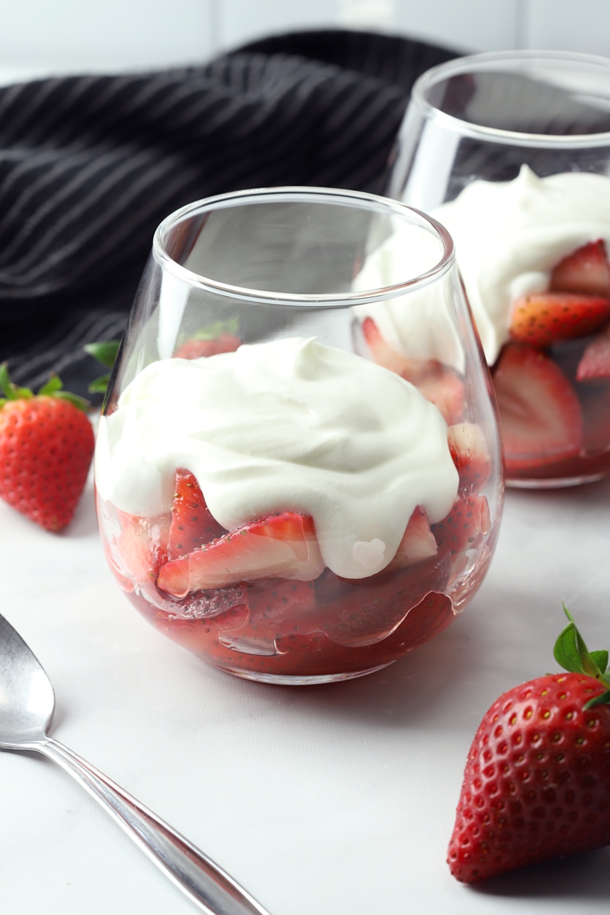 A stemless wine glass with strawberries and cream, with a metal spoon.