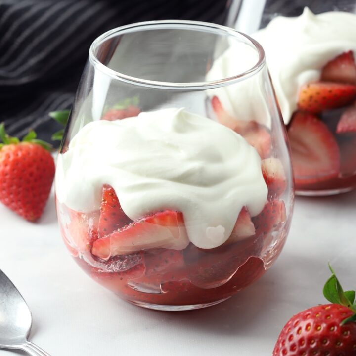 A stemless wine glass filled with strawberries and whipped cream.